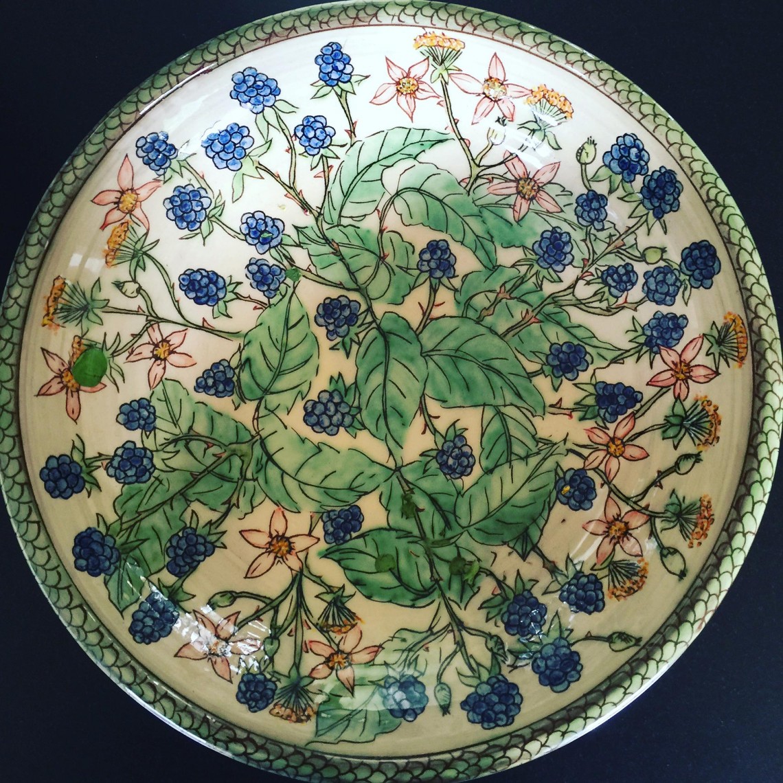 A hand painted pottery charger decorated wild bramble leaves, brambles and pink and yellow wildflowers. Handmade by Peter Thomas of Tower House Pottery, Berwick Upon Tweed, Northumberland